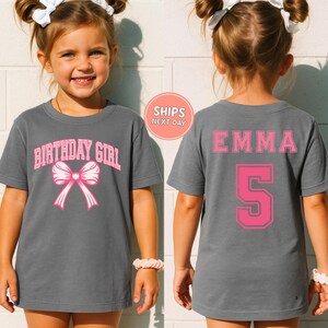 A young girl wearing a gray t-shirt with a pink bow and the text "BIRTHDAY GIRL" printed on it.