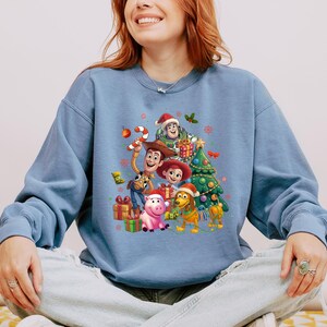 A woman wearing a blue sweatshirt with a cartoon character design on it, smiling and sitting down.