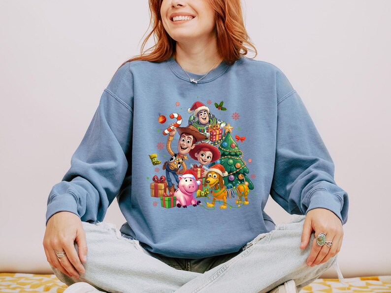 A woman wearing a blue sweatshirt with a cartoon character design on it, smiling and sitting down.