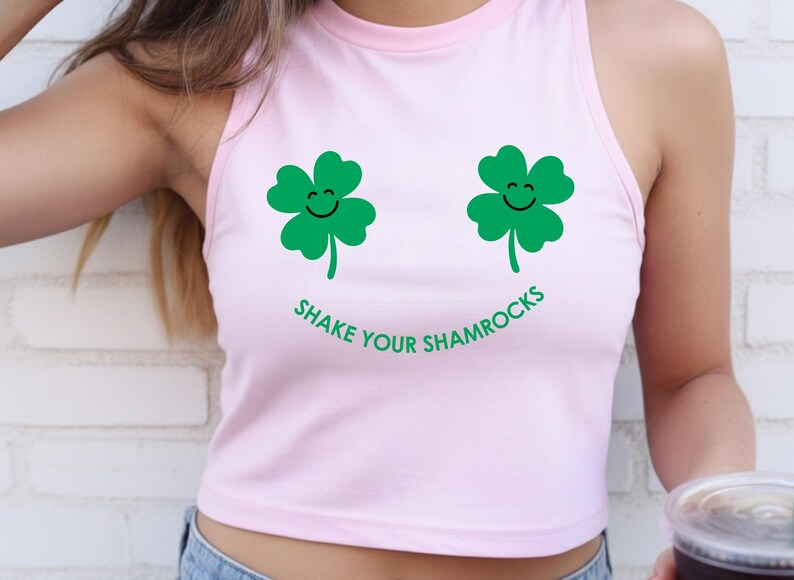 A woman wearing a pink tank top with a graphic of two green shamrocks and the text "SHAKE YOUR SHAMROCKS" printed on it.