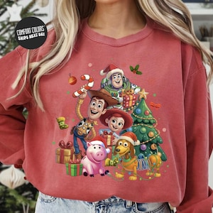 A red sweatshirt with a colorful illustration of characters from the Toy Story movie, including Woody, Buzz Lightyear, and other beloved characters, surrounded by Christmas decorations.