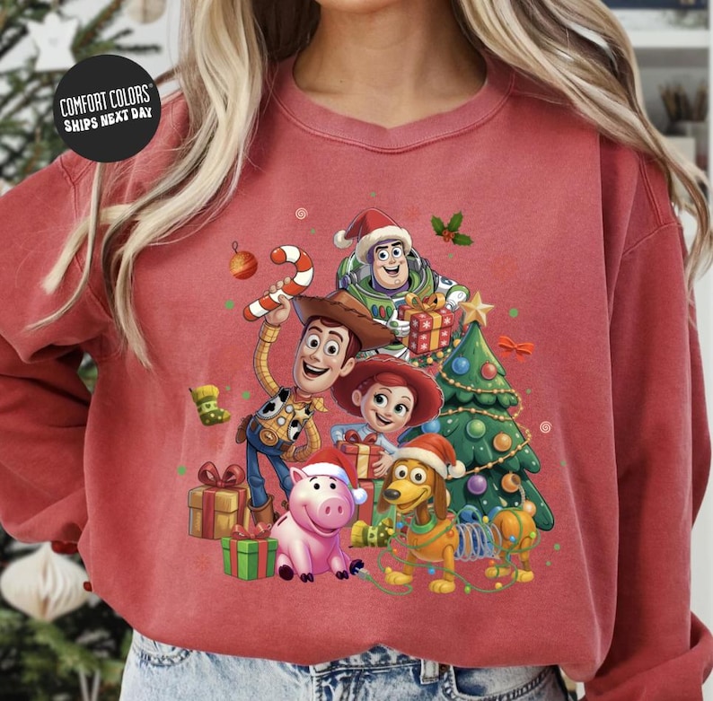 A red sweatshirt with a colorful illustration of characters from the Toy Story movie, including Woody, Buzz Lightyear, and other beloved characters, surrounded by Christmas decorations.