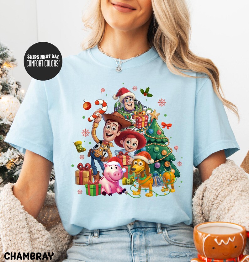 A woman wearing a light blue t-shirt with a colorful graphic of characters from the Toy Story movie, including Woody, Buzz Lightyear, and a pig, surrounded by Christmas decorations.