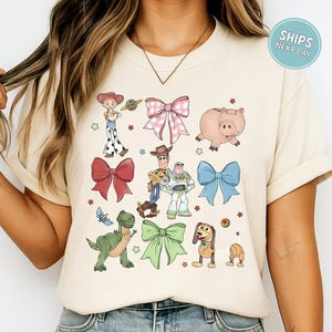 A woman wearing a white t-shirt with a graphic design featuring characters from the Toy Story movie, including Woody, Buzz Lightyear, and other beloved characters.