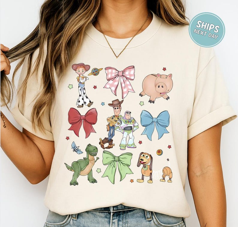 A woman wearing a white t-shirt with a graphic design featuring characters from the Toy Story movie, including Woody, Buzz Lightyear, and other beloved characters.