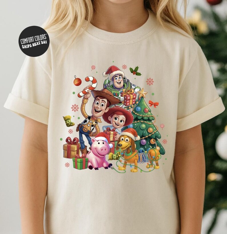 A t-shirt featuring a colorful illustration of characters from the Toy Story movie, including Woody, Buzz Lightyear, and other beloved characters, surrounded by Christmas decorations.