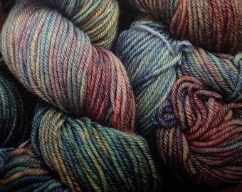May include: Close-up of several skeins of yarn in various colors. The yarn is a mix of greens, blues, reds, and yellows, creating a variegated effect. The texture of the yarn is clearly visible, suggesting a soft, natural fiber. Ideal for knitting or crochet projects.