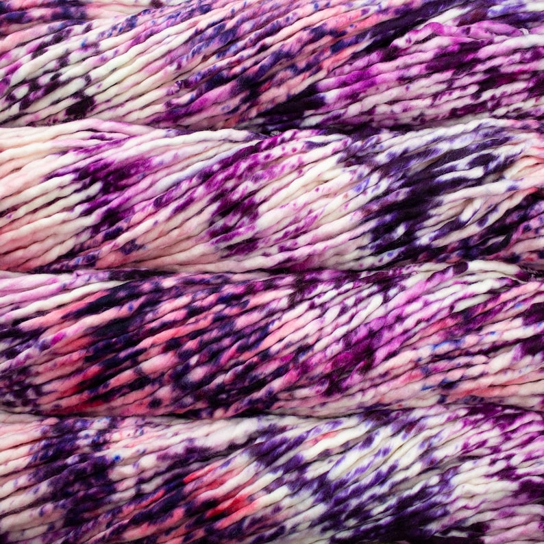 May include: Close-up of thick, hand-dyed yarn in shades of purple, pink, and white. The yarn has a textured, chunky appearance, ideal for knitting or crocheting projects. The color variations create a visually appealing, artistic effect.