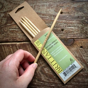 May include: A set of five 7 1/2 inch double-pointed knitting needles made from sustainably harvested birch. The needles are packaged in a brown paper box with the brand name "Brittany" and the text "Knitting Needles Crochet Hooks" printed on the front. The needles are size 10 (6.0 mm).