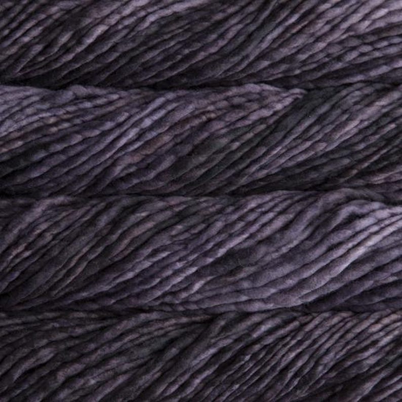 May include: Close-up of a skein of dark purple yarn with a textured, slightly uneven surface. The yarn appears thick and chunky, with variations in color and tone, creating a rich, dimensional appearance. Ideal for knitting and crochet projects.