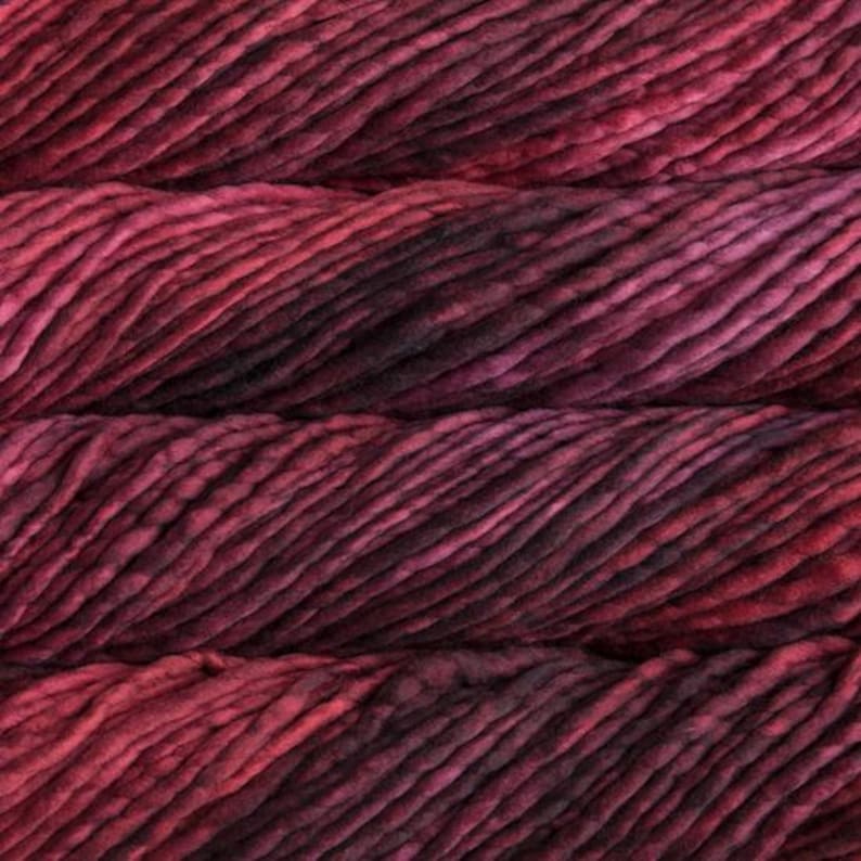 May include: Close-up of a skein of thick, hand-dyed yarn in shades of red and burgundy. The yarn has a textured, chunky appearance, with visible variations in color and tone. Ideal for knitting or crochet projects.