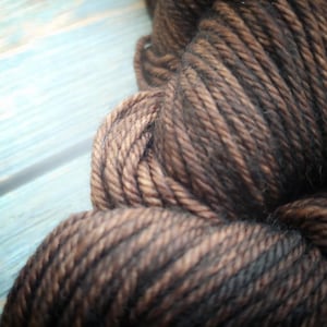 Malabrigo Rios Coco Tonal Espresso Superwash Merino Yarn, a skein of rich brown and black yarn with subtle texture, showcasing the brand's signature quality and color blend, ideal for knitting and crochet projects.