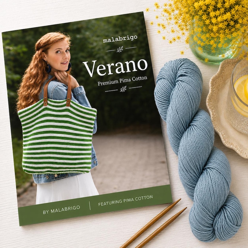 Puede incluir: Un libro de patrones Malabrigo Verano Premium Pima Cotton que muestra un bolso de ganchillo a rayas verdes y blancas con asas de cuero marr&oacute;n, acompa&ntilde;ado de una madeja de hilo azul y dos agujas de tejer de madera sobre una superficie blanca.
