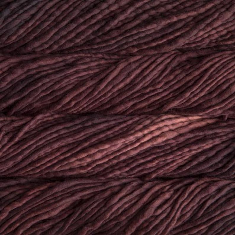 May include: Close-up of thick, burgundy-colored yarn. The yarn is arranged in horizontal rows, with visible texture and variations in color, ranging from deep red to lighter shades. The image highlights the yarn's soft, bulky appearance, suitable for knitting or crocheting projects.