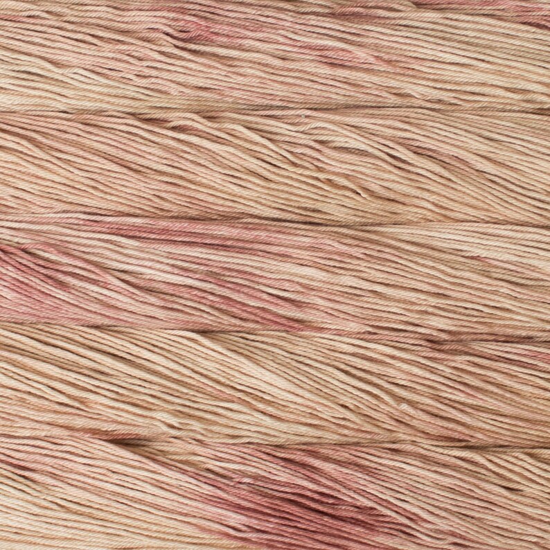 Puede incluir: Una madeja de hilo con una paleta de colores variados en tonos beige suave, crema y rosa empolvado apagado. Las fibras est&aacute;n retorcidas en una estructura de varios cabos, creando una apariencia texturizada y consistente en toda la superficie.