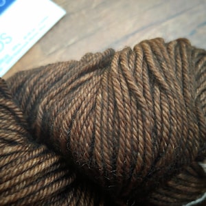 Malabrigo Rios Coco Tonal Espresso Superwash Merino Yarn skein in a rich, dark brown color with subtle espresso tones, showcasing twisted, chunky texture on a wooden surface.