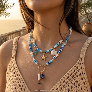 Peut inclure: Un collier superposé composé de perles disques bleues, blanches et turquoise, de petites breloques étoiles de mer blanches, d'un pendentif étoile de mer doré et d'un anneau doré avec des coquillages et perles pendants, sur un haut en crochet beige.