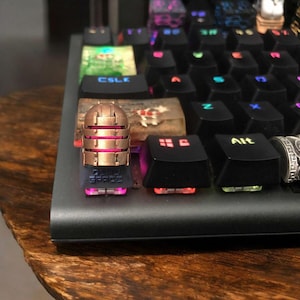 May include: A custom mechanical keyboard with black keycaps and a copper-coloured keycap shaped like a helmet. The keycap has the text "ZERO SPACE" on it. The keyboard has colourful LED backlighting.