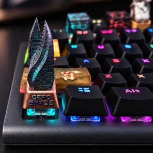 Könnte beinhalten: Eine mechanische Tastatur mit einer individuellen Artisan-Taste in Form eines dunklen, texturierten metallischen Markers aus Dead Space. Die Basis der Taste ist kupferfarben mit der Gravur Dead Space, während andere Tasten schwarze Oberflächen und RGB-Beleuchtung haben.