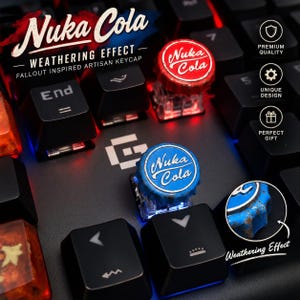 May include: Two artisan keycaps shaped like bottle caps, one red and one blue, both featuring the Nuka Cola logo and a weathered, rusted finish. These keycaps are installed on a black mechanical keyboard with red and blue backlighting.