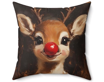 May include: Square pillow featuring a close-up of a reindeer with a bright red nose, brown antlers, and large, expressive eyes. The reindeer has a cheerful expression and is set against a dark background. The pillow is a festive holiday decoration.