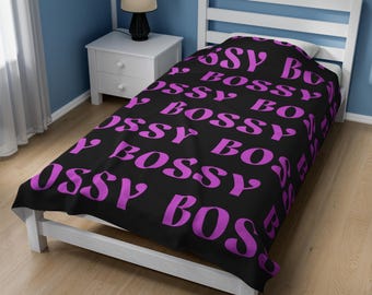 Può includere: Un lenzuolo per letto matrimoniale nero con un motivo ripetitivo della parola "Bossy" in lettere rosa.