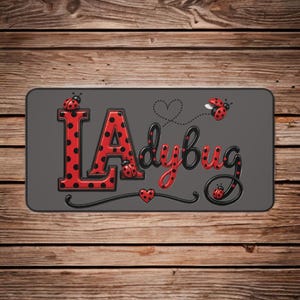 May include: A rectangular sign with the words "Ladybug" in red and black. The letters "LA" are red with black polka dots, and the word "dybug" is in a cursive font. Ladybug illustrations and heart accents complete the design.