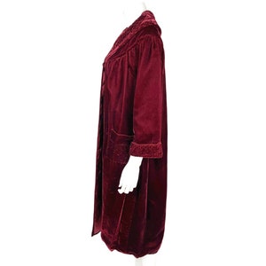 May include: A long, burgundy velvet robe with a shawl collar and a tie belt. The robe has a quilted pattern and is trimmed with a contrasting fabric.