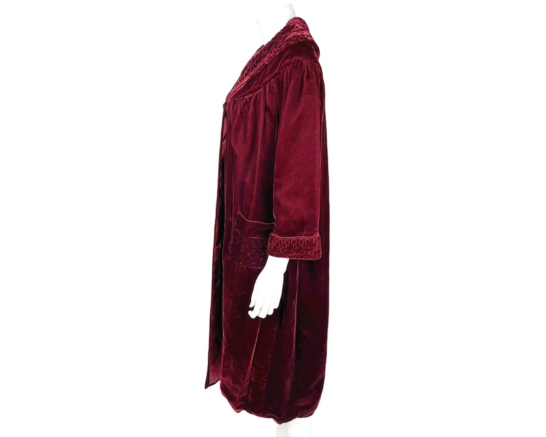 May include: A long, burgundy velvet robe with a shawl collar and a tie belt. The robe has a quilted pattern and is trimmed with a contrasting fabric.