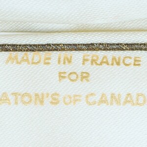 May include: A white fabric label with gold text that reads "Made in France for Eaton's of Canada".