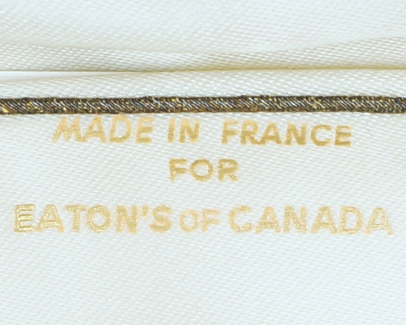 May include: A white fabric label with gold text that reads "Made in France for Eaton's of Canada".