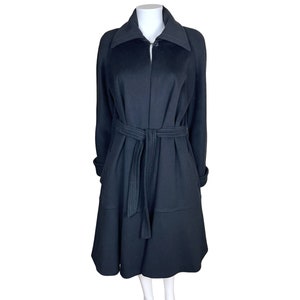 Pode incluir: Um casaco preto com gola larga e cinto a condizer. O casaco tem mangas compridas e bainha até ao joelho. O cinto é cosido com linha branca. O casaco é exibido num manequim branco.