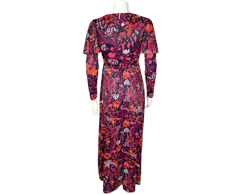 May include: A floor-length dress featuring a vibrant floral pattern in shades of dark blue, bright red, orange, and white. The garment has long sleeves with flared cuffs, a fitted waist, and a concealed zipper closure along the center back.