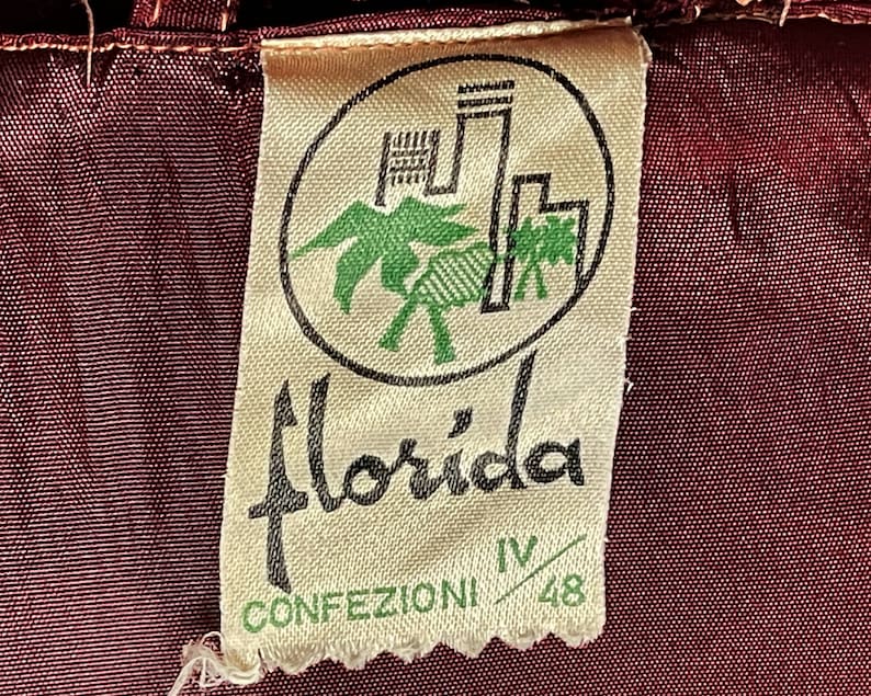 May include: A white tag with a black and green logo of a palm tree and a building. The text "Florida Confezioni IV/48" is printed on the tag.