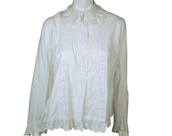 May include: A white long-sleeved blouse with a ruffled collar and decorative embroidery down the front and along the hem. The blouse has a button-down front and a relaxed fit, suitable for various occasions.