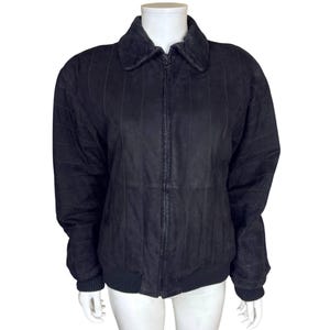 May include: A black suede jacket with a zip-up front and a ribbed hem and cuffs. The jacket has a collared neckline and vertical stitched detailing. The jacket is displayed on a white mannequin.