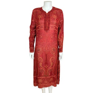 May include: A long-sleeved, knee-length dress in a vibrant red hue, adorned with an intricate paisley pattern in shades of gold and brown. The dress features a mandarin collar and a button-down front, showcasing a detailed, all-over design.