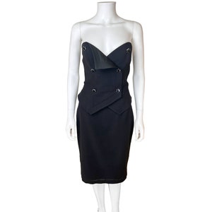 May include: A black strapless dress with a fitted bodice and a skirt that falls to the knee. The bodice has a unique design with a folded flap and buttons.