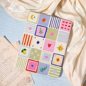 May include: A rectangular tablet case featuring a grid of colorful squares with various illustrations including a yellow lemon, red hearts, pink lips, orange suns, blue stars, green leaves, and striped patterns in shades of blue, green, pink, and cream.