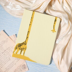 May include: A rectangular tablet case in a pale yellow color featuring a graphic illustration of a giraffe with an elongated neck that stretches across the front cover, with the giraffe's head appearing near the top right corner of the case.