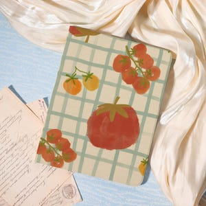 May include: A tablet case featuring a watercolor illustration of tomatoes and a checkered pattern in shades of red, orange, and green. The design includes a large tomato and clusters of smaller tomatoes.