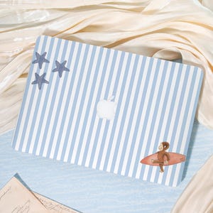 May include: Laptop skin with a blue and white striped pattern, featuring three blue starfish and a cartoon monkey riding a red surfboard. The Apple logo is visible. The skin is designed to fit a laptop.