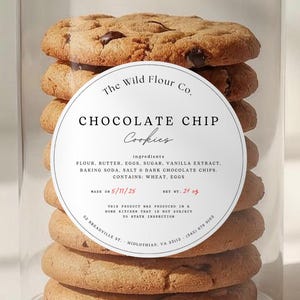 Puede incluir: Un recipiente transparente lleno de galletas con chispas de chocolate. Las galletas están apiladas y tienen un color marrón dorado con chispas de chocolate visibles. Una etiqueta blanca con texto está en el recipiente. La etiqueta dice "Chocolate Chip Cookies".