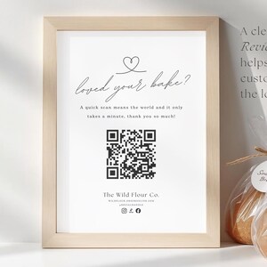 May include: A framed sign with the text "loved your bake?" and a QR code, next to three loaves of sourdough bread in clear bags with tags. The sign is in a light wood frame, and the bread is tied with twine.
