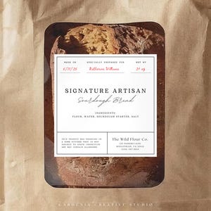 May include: A brown paper bag with a clear window displaying a loaf of sourdough bread. The label reads "Signature Artisan Sourdough Bread" with ingredients listed. The bag also includes the text "The Wild Flour Co."