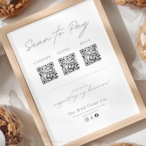 May include: A framed sign with the text "Scan to Pay" and QR codes for CashApp, Venmo, and Zelle. The sign also includes the text "thank you for supporting my business" and the business name, "The Wild Flour Co.". Chocolate chip cookies are in the background.