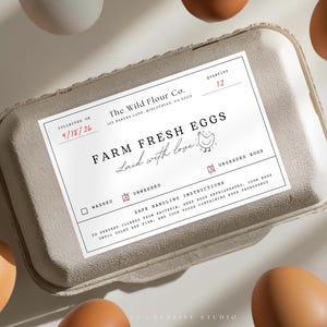May include: A rectangular gray cardboard egg carton with a white label featuring the text The Wild Flour Co., Farm Fresh Eggs, Laid with love, and safe handling instructions. The label indicates a quantity of 12 and is surrounded by brown eggs.