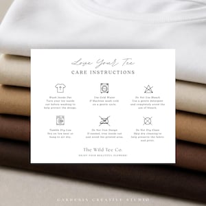 Op de afbeelding: Een stapel van vijf gevouwen t-shirts in de kleuren wit, beige, zand, lichtbruin en donkerbruin. Bovenop ligt een witte rechthoekige kaart met wasvoorschriften, voorzien van zwarte tekst en iconen voor het wassen, drogen en strijken.