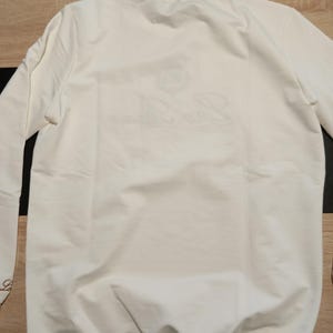 K&ouml;nnte beinhalten: Eine wei&szlig;e Keramik-Tasse mit schwarzem Henkel und dem Text "But First, Coffee" in handschriftlichem Stil. Die Tasse steht auf einer wei&szlig;en Oberfl&auml;che. Die Tasse ist etwa 10 cm hoch.