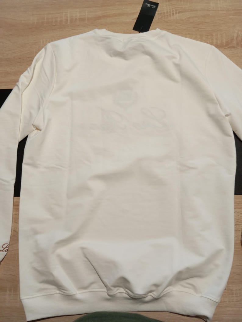 K&ouml;nnte beinhalten: Eine wei&szlig;e Keramik-Tasse mit schwarzem Henkel und dem Text "But First, Coffee" in handschriftlichem Stil. Die Tasse steht auf einer wei&szlig;en Oberfl&auml;che. Die Tasse ist etwa 10 cm hoch.